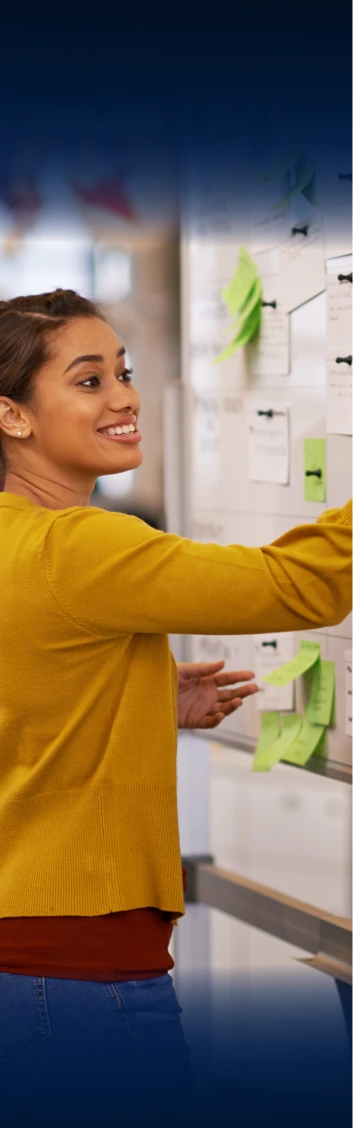 Smiling woman in yellow top placing sticky notes on a whiteboard in a bright office