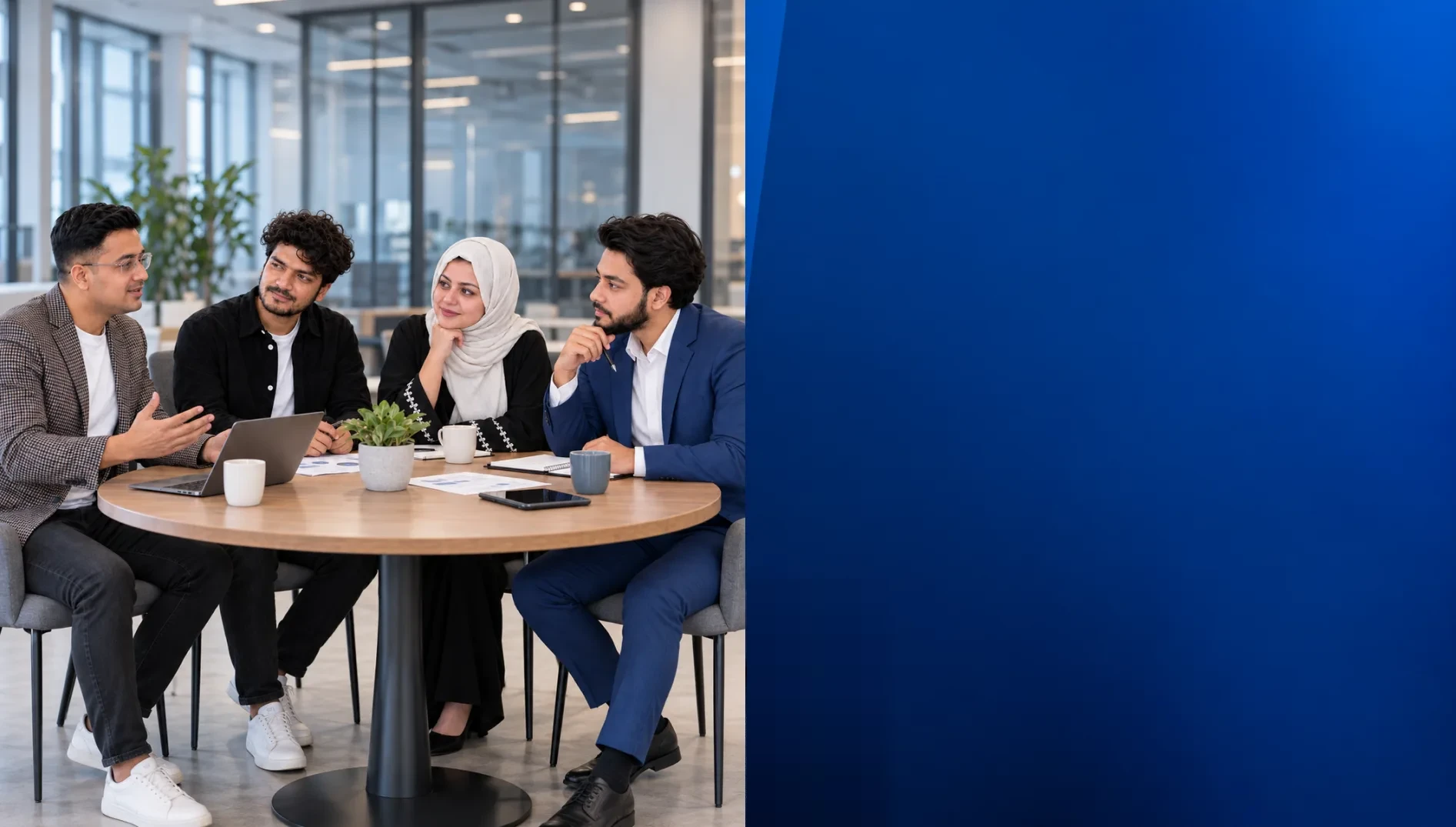 Four colleagues in discussion around a round table with a laptop in a bright office
