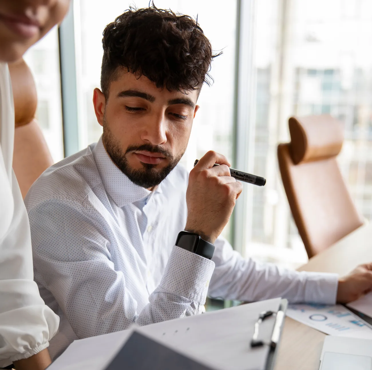 Thoughtful young professional holding a marker while reviewing printed charts at a meeting table