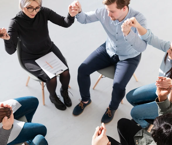 Colleagues sitting in a circle on chairs, holding hands up together in a support group