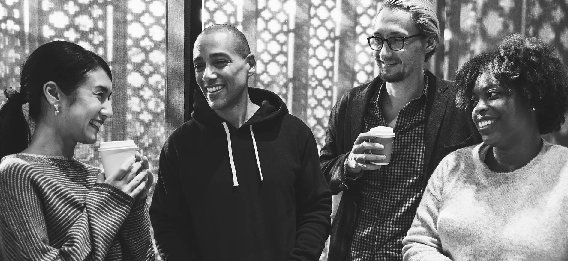Four smiling colleagues chatting over takeaway coffee