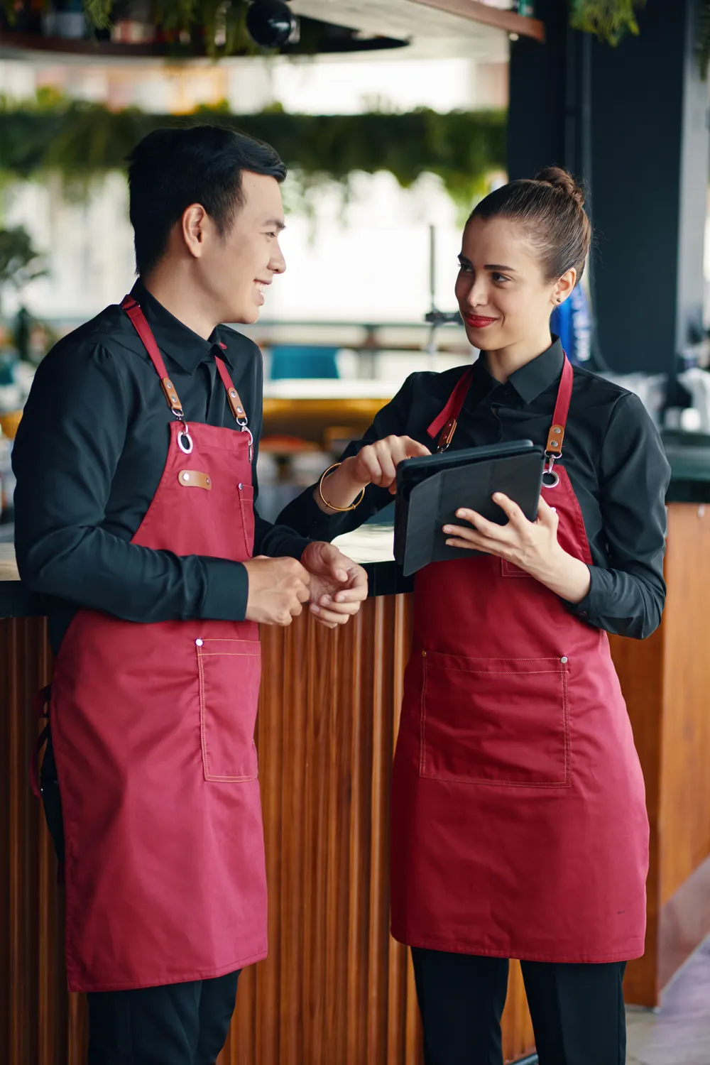 Two restaurant staff in red aprons reviewing orders on a tablet