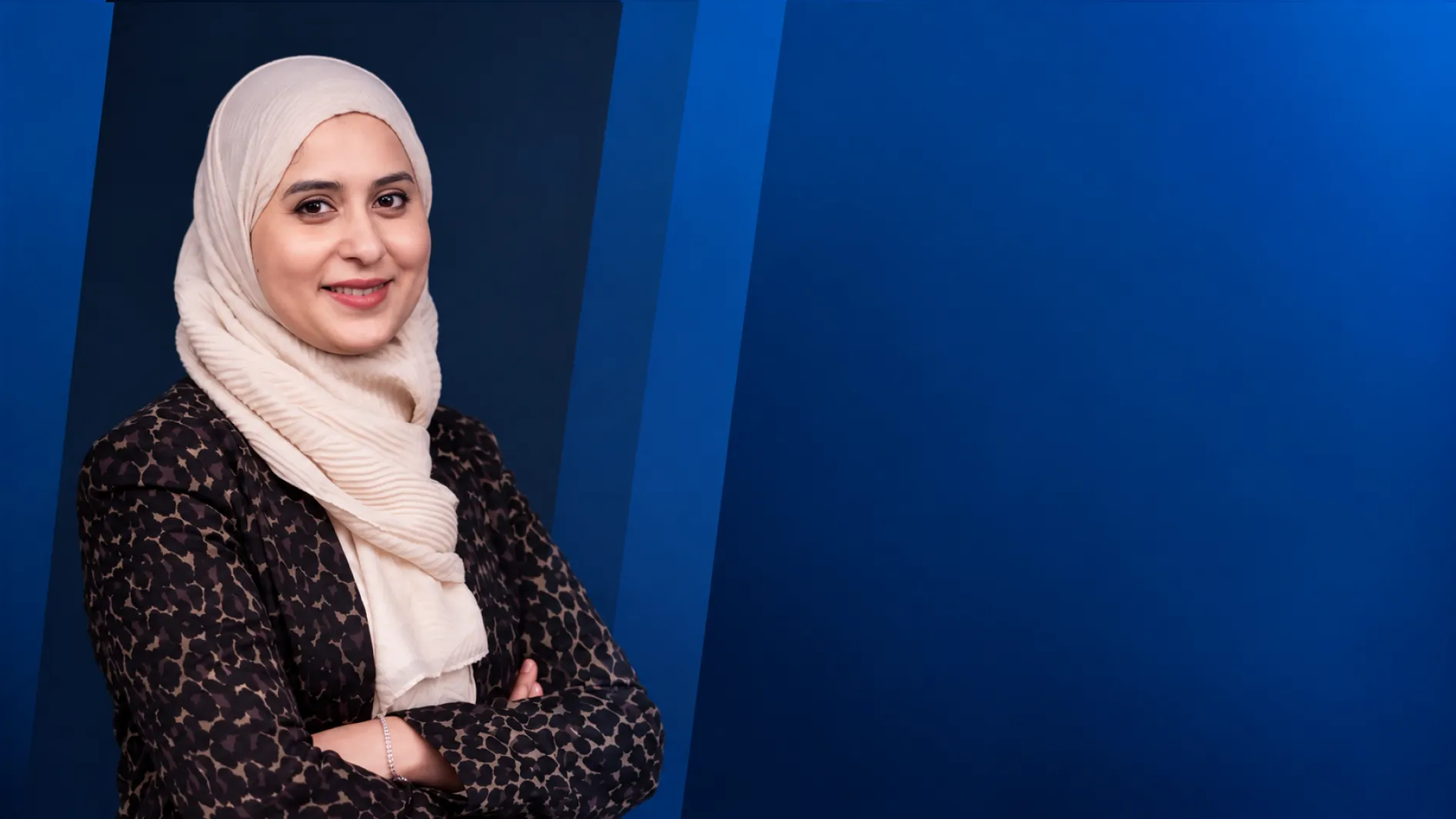 Madiha Alam, HR Management Solution Advisor, smiling with arms crossed against a blue background