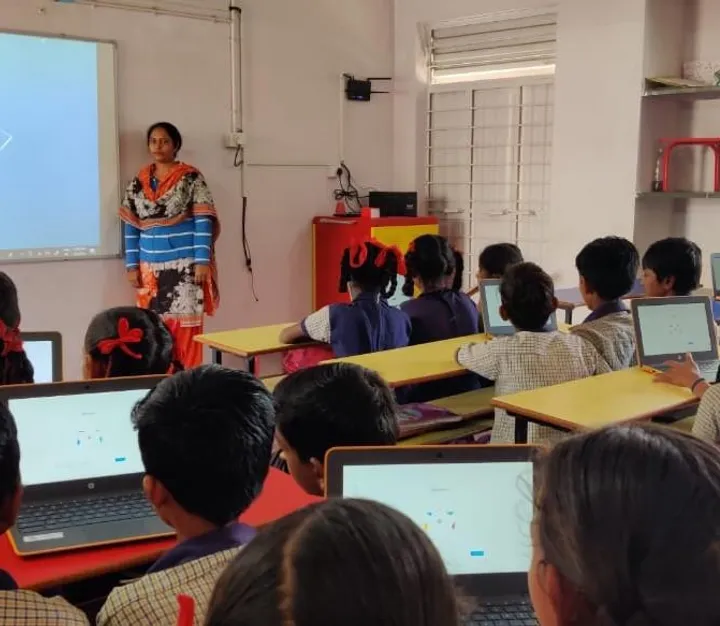 Students on laptops watching a teacher present on a projector