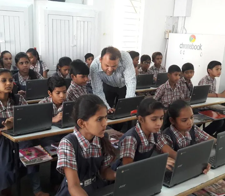 Teacher helping schoolchildren working on laptops