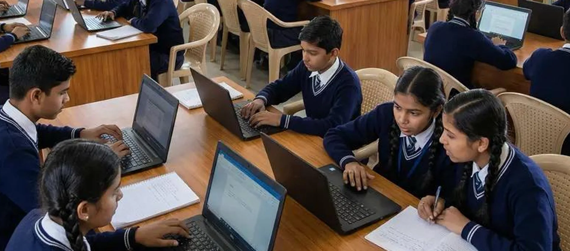 Students in school uniform working on laptops at shared desks in a classroom