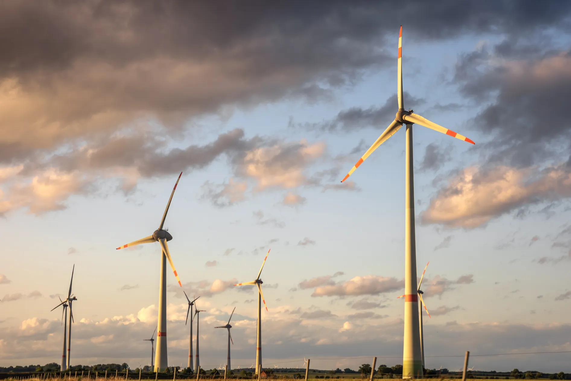 Wind turbines on farmland under a cloudy golden-hour sky