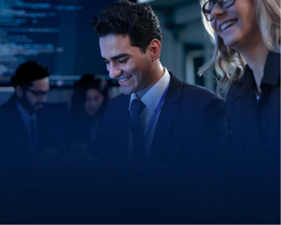 Two smiling professionals in business suits looking at a screen in a tech office