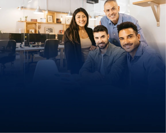 Four diverse smiling office colleagues posing together in a modern open workspace