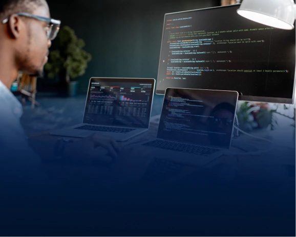 Developer with glasses reviewing code and data dashboards on multiple screens