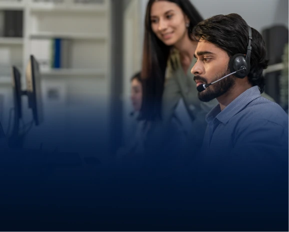 Male IT support agent with headset at a monitor with a female colleague beside him