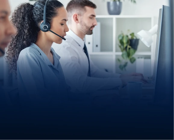 Two IT support professionals wearing headsets working at computers in a bright office