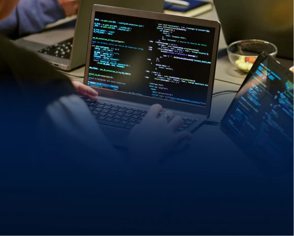 Developer typing on a laptop with colourful code visible on screen in a dim room