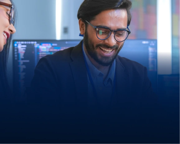 Smiling male developer with glasses sitting in front of monitors with code
