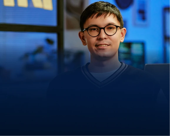 Young male developer with glasses smiling in a blue-lit tech workspace